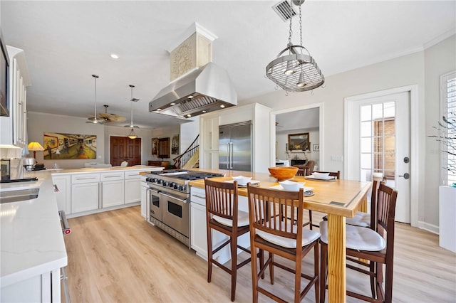 kitchen featuring decorative light fixtures, white cabinets, premium appliances, light stone counters, and light hardwood / wood-style flooring