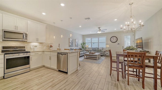 kitchen with kitchen peninsula, appliances with stainless steel finishes, decorative light fixtures, and white cabinetry