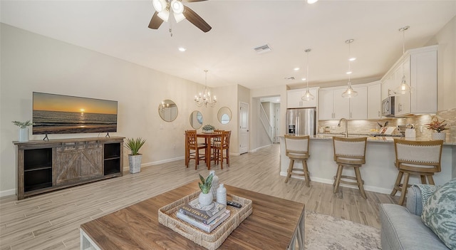 living room with sink, light hardwood / wood-style floors, and ceiling fan with notable chandelier