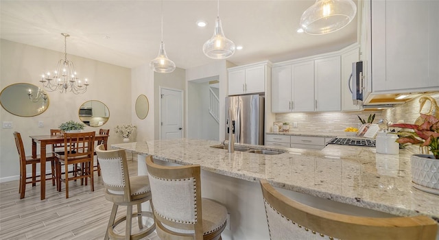 kitchen featuring a breakfast bar area, light hardwood / wood-style flooring, decorative light fixtures, white cabinetry, and stainless steel appliances