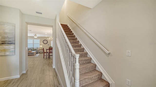 stairway featuring wood-type flooring and ceiling fan with notable chandelier