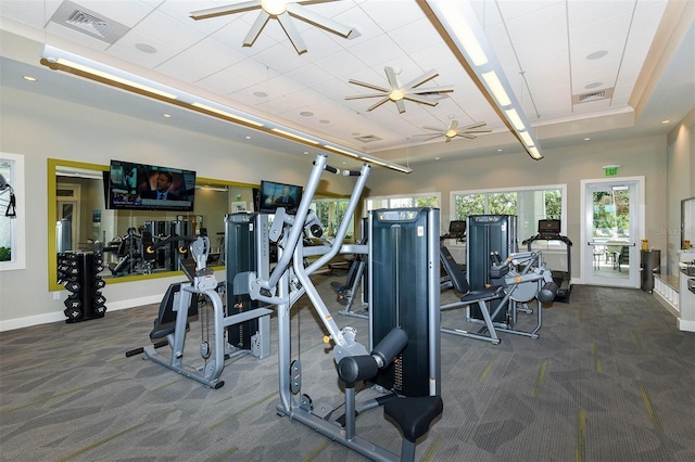 gym featuring dark colored carpet, a tray ceiling, and ceiling fan