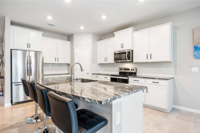 kitchen featuring sink, dark stone countertops, a center island with sink, white cabinets, and appliances with stainless steel finishes