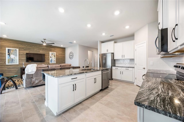 kitchen featuring a kitchen island with sink, white cabinets, sink, wooden walls, and stainless steel appliances