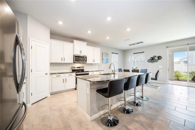 kitchen featuring white cabinetry, sink, dark stone countertops, a kitchen island with sink, and appliances with stainless steel finishes