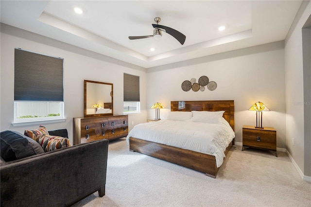 carpeted bedroom featuring a raised ceiling, multiple windows, and ceiling fan