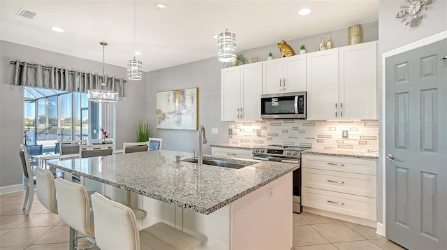 kitchen featuring appliances with stainless steel finishes, light stone counters, a kitchen island with sink, sink, and white cabinets