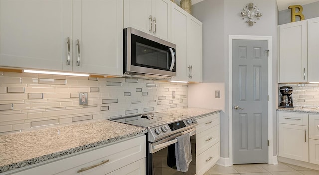 kitchen with stainless steel appliances, light tile patterned floors, tasteful backsplash, light stone counters, and white cabinets