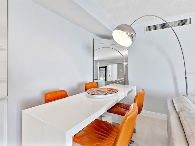 dining area with visible vents, light wood-style floors, baseboards, and a textured ceiling