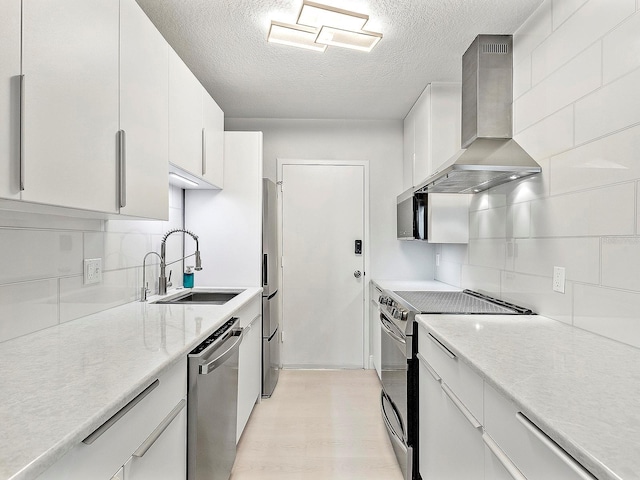 kitchen with wall chimney range hood, decorative backsplash, light wood-style flooring, appliances with stainless steel finishes, and a sink