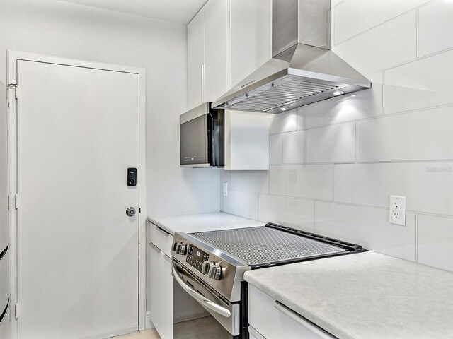 kitchen featuring stainless steel electric stove, white cabinets, light countertops, and wall chimney range hood