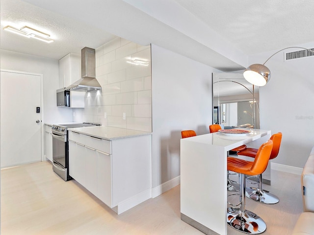 kitchen with visible vents, wall chimney range hood, a breakfast bar area, stainless steel electric range oven, and decorative backsplash