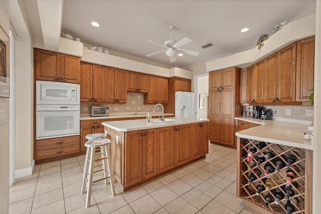 kitchen featuring backsplash, an island with sink, white appliances, a breakfast bar area, and light tile patterned flooring