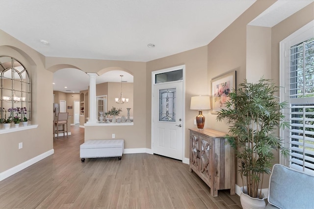 foyer with light wood-type flooring, decorative columns, and a notable chandelier