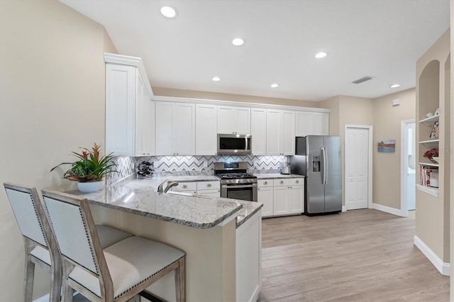 kitchen featuring kitchen peninsula, light hardwood / wood-style flooring, light stone countertops, white cabinetry, and stainless steel appliances