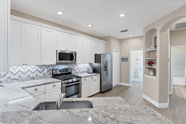 kitchen featuring light stone countertops, appliances with stainless steel finishes, light wood-type flooring, sink, and white cabinetry