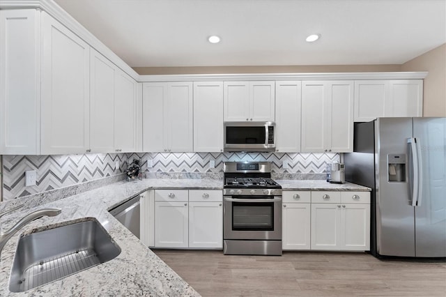 kitchen with light wood-type flooring, light stone counters, stainless steel appliances, sink, and white cabinetry