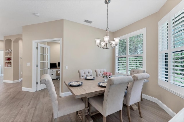 dining area with light wood-type flooring, plenty of natural light, and a notable chandelier