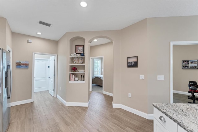 kitchen featuring white cabinets, stainless steel fridge with ice dispenser, light hardwood / wood-style floors, and light stone counters