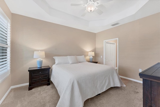 bedroom with ceiling fan, a raised ceiling, light carpet, and a closet