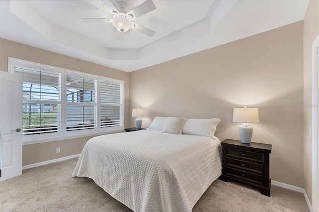 carpeted bedroom with ceiling fan and a tray ceiling