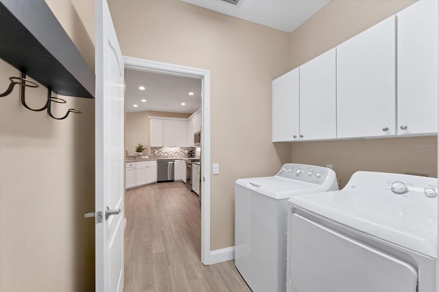 laundry room featuring washer and dryer, cabinets, and light hardwood / wood-style flooring