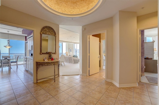 corridor featuring a tray ceiling, a wealth of natural light, and light tile patterned floors