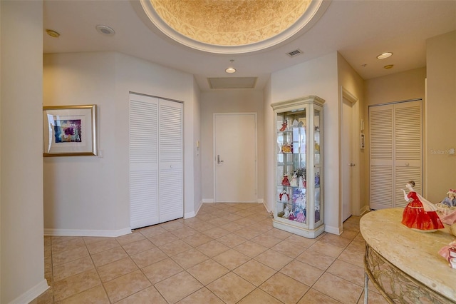 corridor with light tile patterned flooring and a tray ceiling