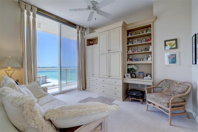 living area with a water view, plenty of natural light, light colored carpet, and ceiling fan