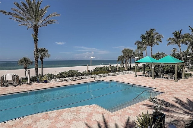 view of pool featuring a gazebo, a patio area, a water view, and a view of the beach