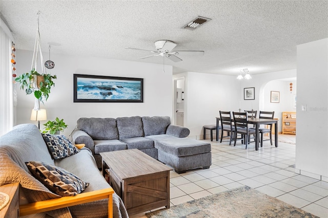 tiled living room with ceiling fan with notable chandelier and a textured ceiling