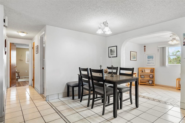 dining area featuring ceiling fan with notable chandelier, light tile patterned floors, and a textured ceiling