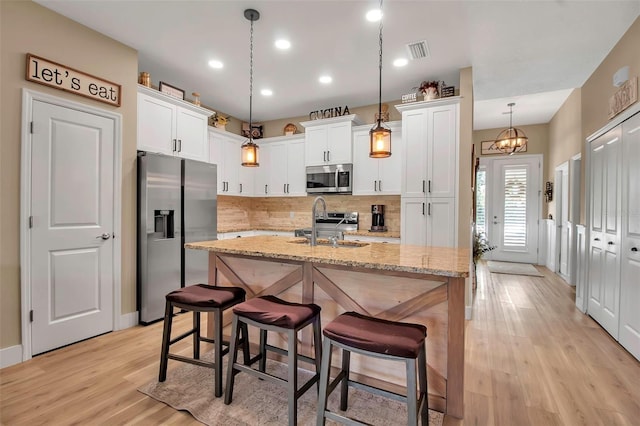 kitchen featuring a kitchen island with sink, white cabinetry, pendant lighting, and appliances with stainless steel finishes