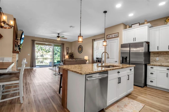 kitchen featuring appliances with stainless steel finishes, a breakfast bar, a kitchen island with sink, sink, and white cabinetry