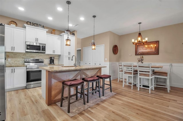 kitchen featuring a kitchen island with sink, sink, light wood-type flooring, appliances with stainless steel finishes, and white cabinetry