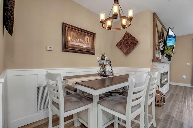 dining space with a fireplace, light wood-type flooring, and a notable chandelier