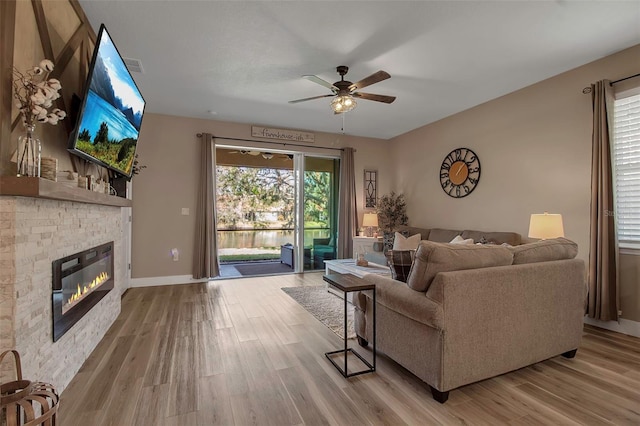 living room with light hardwood / wood-style floors, a stone fireplace, and ceiling fan