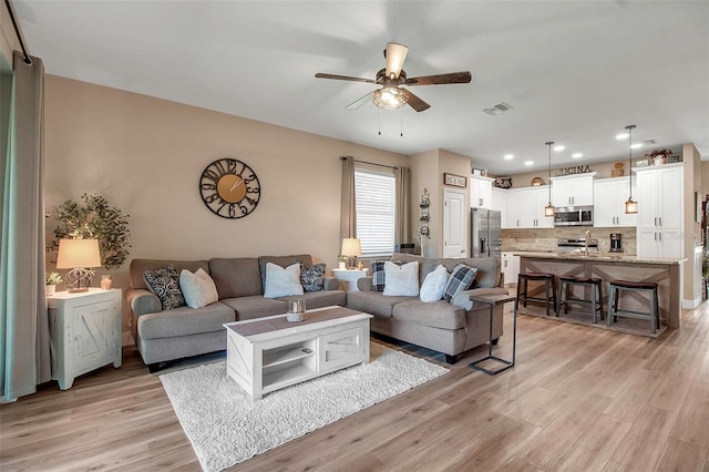 living room with ceiling fan, sink, and light wood-type flooring