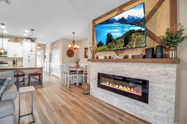 living room with light wood-type flooring, a stone fireplace, and an inviting chandelier