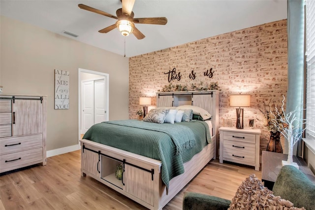 bedroom with ceiling fan, light hardwood / wood-style floors, brick wall, and a closet