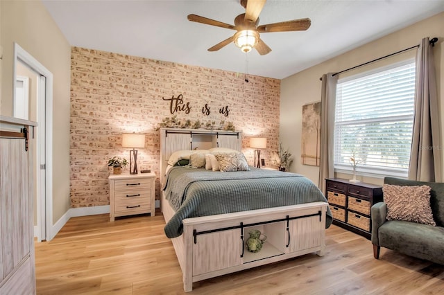 bedroom with light wood-type flooring, ceiling fan, and brick wall