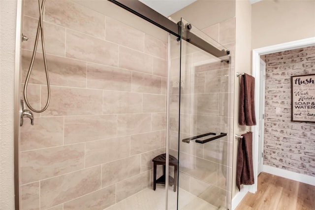 bathroom featuring wood-type flooring, a shower with shower door, and brick wall