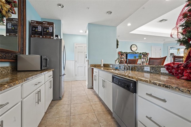 kitchen featuring appliances with stainless steel finishes, sink, light tile patterned floors, dark stone countertops, and white cabinetry