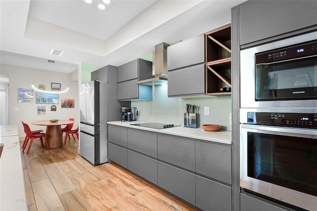 kitchen featuring gray cabinets, light hardwood / wood-style flooring, stainless steel appliances, and wall chimney range hood