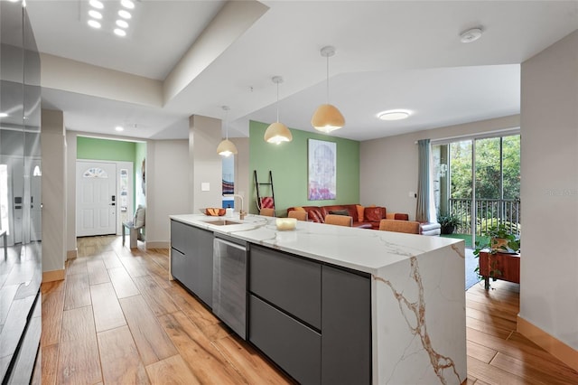 kitchen featuring pendant lighting, gray cabinetry, sink, light wood-type flooring, and an island with sink