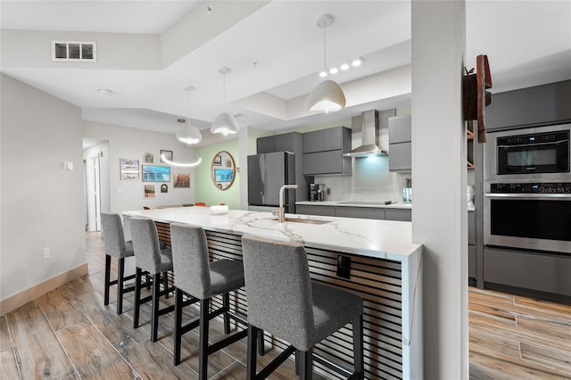 kitchen with a breakfast bar area, gray cabinets, stainless steel refrigerator, and wall chimney exhaust hood