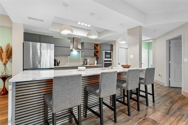 kitchen featuring appliances with stainless steel finishes, decorative light fixtures, a kitchen breakfast bar, and wall chimney exhaust hood