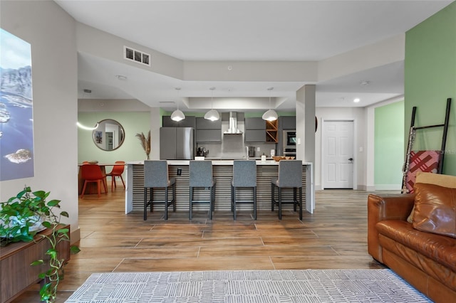 kitchen featuring a kitchen bar, stainless steel fridge, kitchen peninsula, wall chimney range hood, and hanging light fixtures