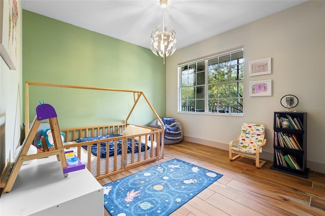 bedroom with an inviting chandelier, a nursery area, and hardwood / wood-style flooring