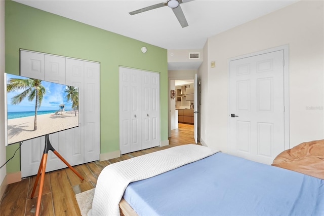 bedroom featuring two closets, ceiling fan, and hardwood / wood-style flooring